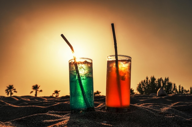 Bevande alcoliche con una cannuccia nella sabbia con palme sullo sfondo
