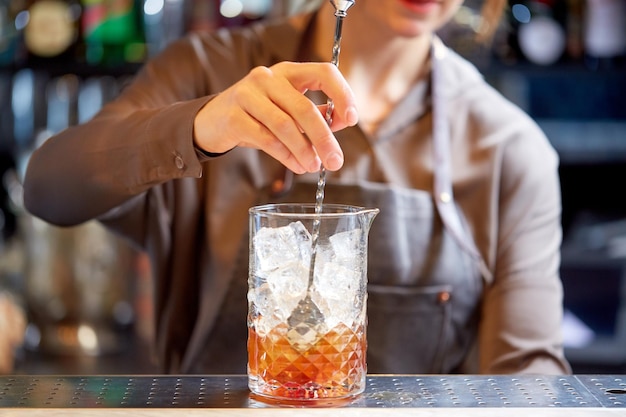 bevande alcoliche, persone e concetto di lusso - barista donna con agitatore e bicchiere che prepara un cocktail al bancone del bar