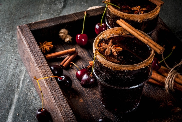 Bevande autunnali e invernali. Sangria di ciliegie calde con cannella, anice, vino e spezie. Su una pietra scura e di legno con ingredienti, nel vassoio