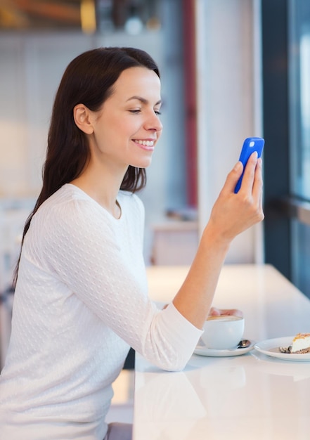 bevande, cibo, persone, tecnologia e concetto di stile di vita - giovane donna sorridente con smartphone che beve caffè al bar