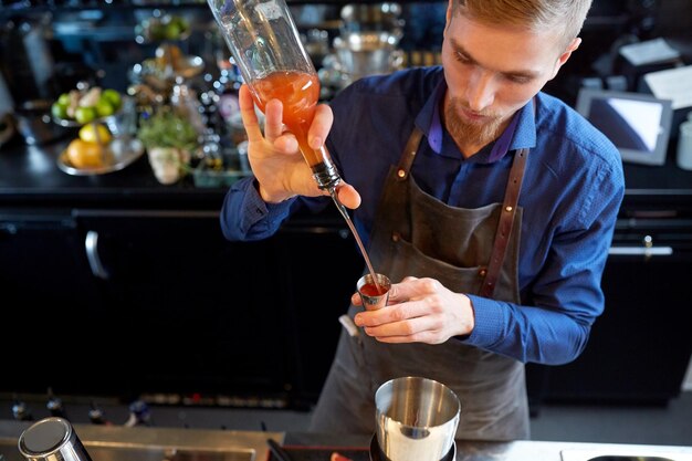 bevande, persone e concetto di lusso: barista con shaker che versa alcol dalla bottiglia nel jigger e prepara un cocktail al bar