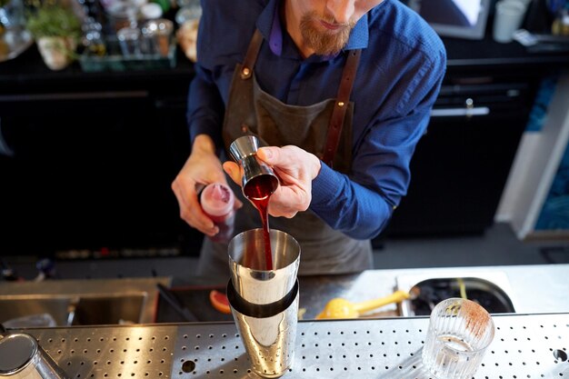 bevande, persone e concetto di lusso: il barista versa alcol dal jigger nello shaker e prepara un cocktail al bar