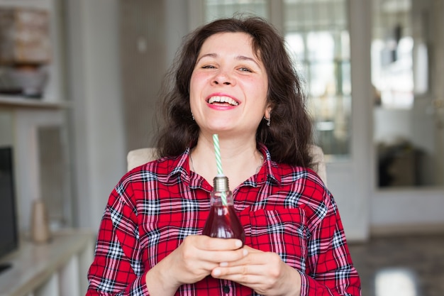 Bevande, persone e concetto di stile di vita. Primo piano di donna felice che beve cola con paglia a casa.