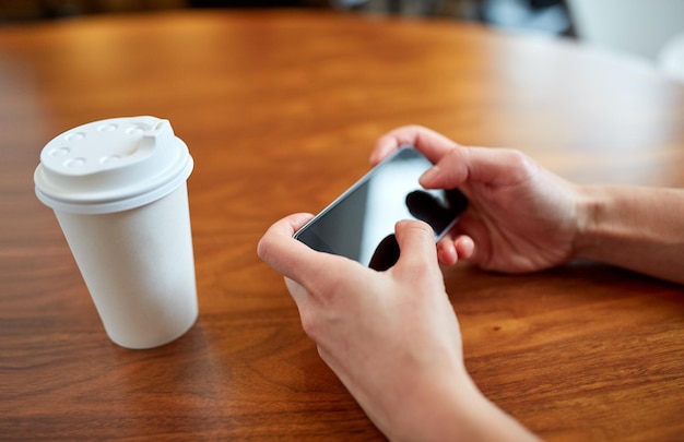 bevande, persone, tecnologia e concetto di stile di vita - primo piano di una donna con smartphone e caffè al tavolo del caffè