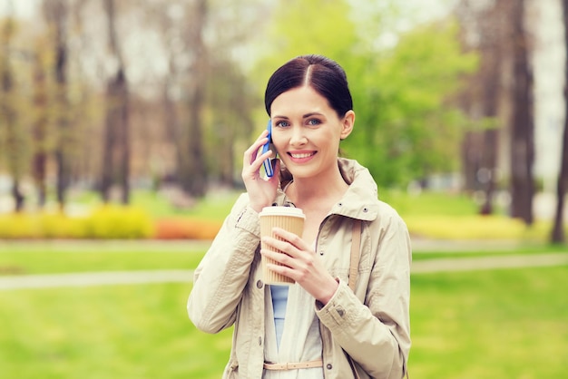 bevande, tempo libero, tecnologia e concetto di persone - donna sorridente con caffè che chiama e parla su smartphone nel parco