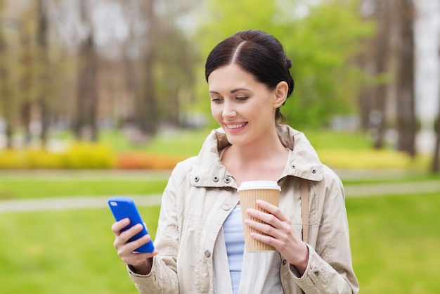 bevande, tempo libero, tecnologia e concetto di persone - donna sorridente con messaggio di sms smartphone e caffè nel parco