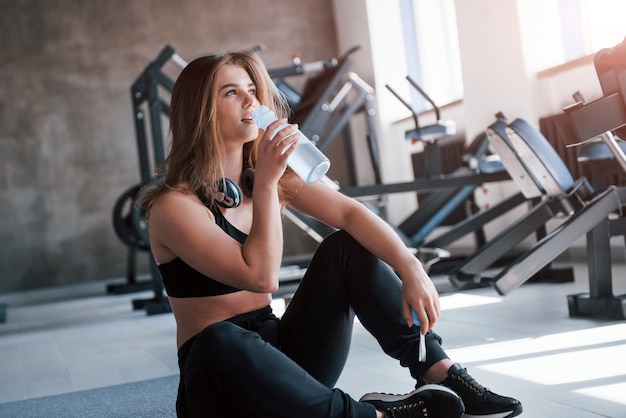 Bevendo acqua. splendida donna bionda in palestra durante il fine settimana.