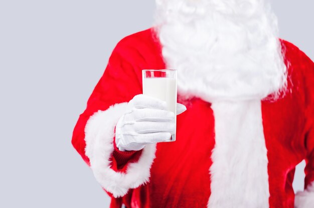 Bevi latte fresco! Babbo Natale tradizionale che allunga la mano con un bicchiere di latte mentre si trova su uno sfondo grigio