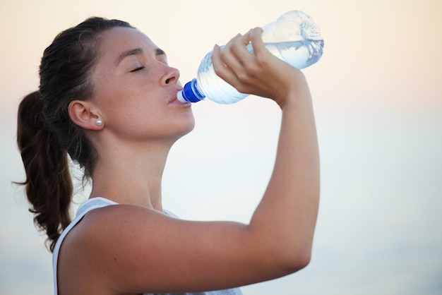 Bevi più acqua il tuo corpo ti ringrazierà per questo Scatto di una giovane donna sportiva che beve acqua mentre è fuori per una corsa