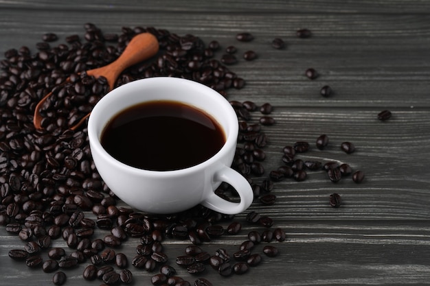 Bianco tazza di caffè nero con fagioli e cucchiaio di legno sul tavolo di legno vintage scuro