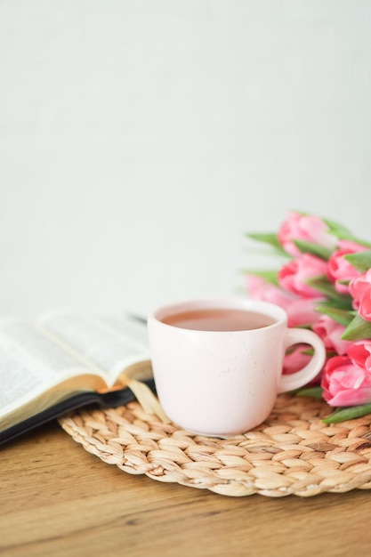 Bibbia aperta con fiori di tulipano e una tazza di tè su legno chiaro
