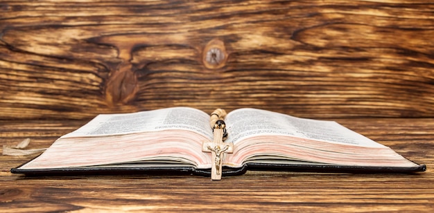 Bibbia aperta con i grani del rosario su fondo di legno
