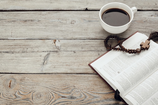 Bibbia e un crocifisso su un vecchio tavolo di legno con una tazza di caffè