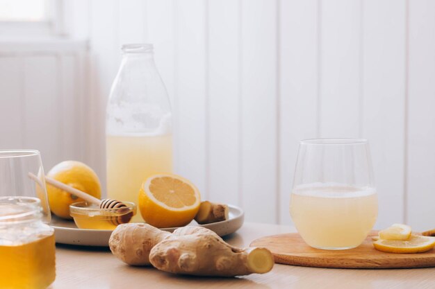 Bicchiere con bevanda a base di ingredienti freschi di radice di zenzero per la sua preparazione tavolo da cucina miele limone