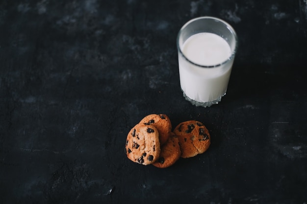 Bicchiere con latte fresco e biscotti con scaglie di cioccolato su superficie scura