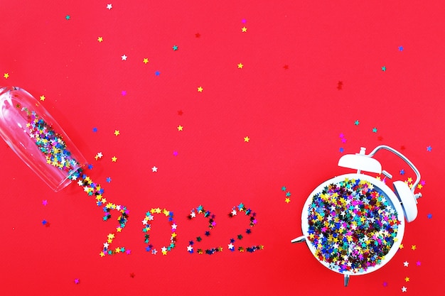 Bicchiere con sveglia di paillettes multicolori e confettie su fondo rosso