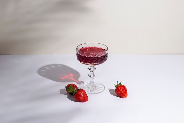 Bicchiere con vino rosso e fragole sul tavolo su sfondo chiaro
