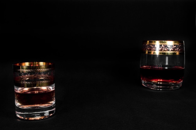 Bicchiere corto e bicchiere di brandy di whisky rosso scuro o xAbourbon isolato su sfondo nero Foto in primo piano dell'alcol