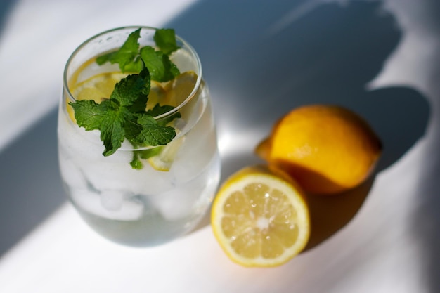 bicchiere d'acqua con menta, limone e ghiaccio su tavola bianca, sfondo giallo