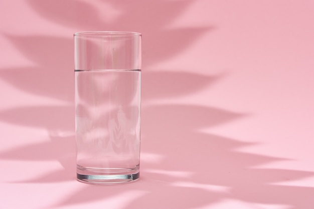 Bicchiere d'acqua e ombra foglia sul rosa