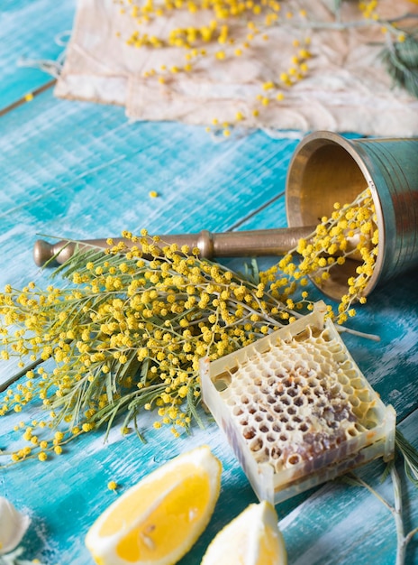 Bicchiere d'acqua, fiori di mimosa, nido d'ape e pezzi di limone su una superficie di legno. Avvicinamento