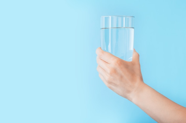 Bicchiere d'acqua in mano femminile sullo spazio della copia del fondo blu di colore. Concetto di fitness stile di vita sano