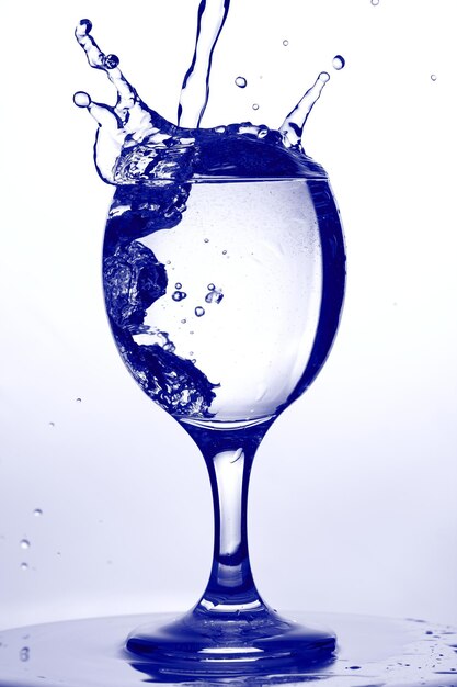 Bicchiere d'acqua. Spruzzi d'acqua nel bicchiere di vino su sfondo blu