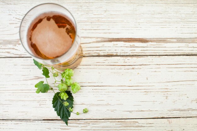 Bicchiere da birra con foglie e coni di luppolo di birra su sfondo tavolo in legno vintage con vista dall'alto dello spazio di copia