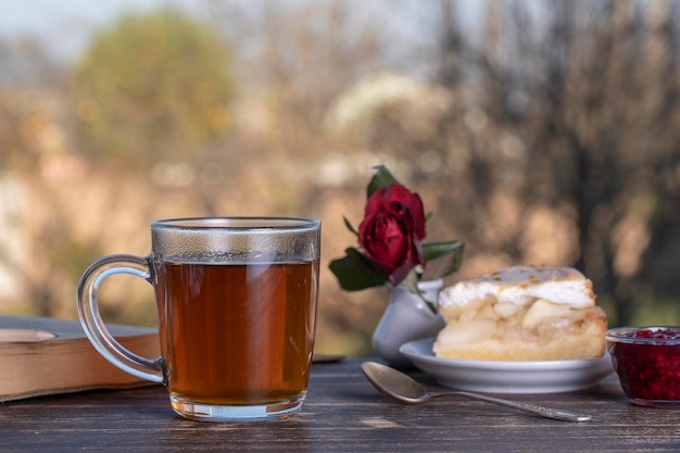 Bicchiere da tè con torta dolce e libro sul tavolo di legno al mattino all'aperto si chiuda