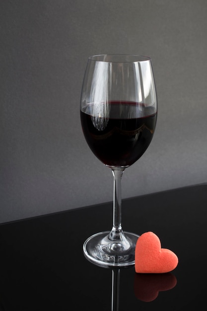 Bicchiere da vino con vino rosso e biscotto a forma di cuore rosso su sfondo scuro. Avvicinamento. Posizione verticale.