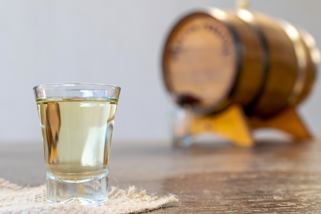 Bicchiere di alcol distillato di alta qualità e vecchia botte di rovere sfocata