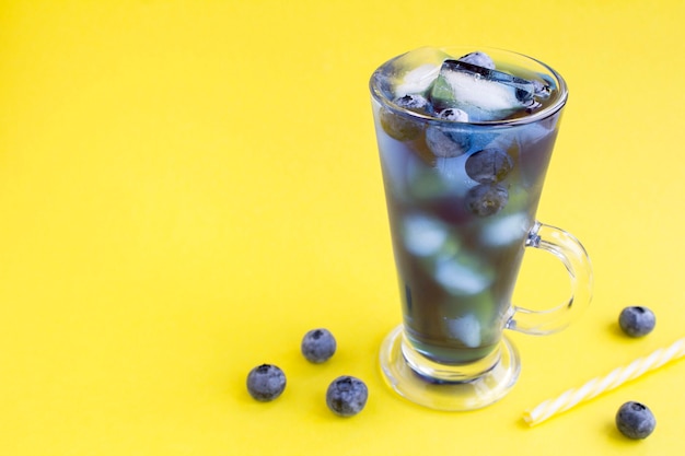 Bicchiere di bevanda cocktail blu con ghiaccio e mirtillo su giallo