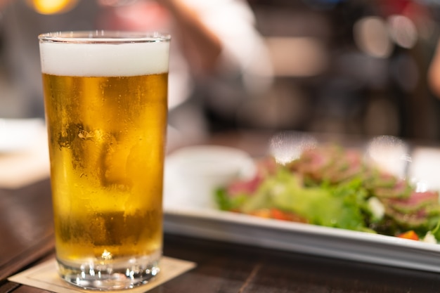 Bicchiere di birra artigianale fredda con bolle bianche e cibo sfocato come sfondo