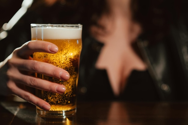 Bicchiere di birra chiara con schiuma nella mano di una donna