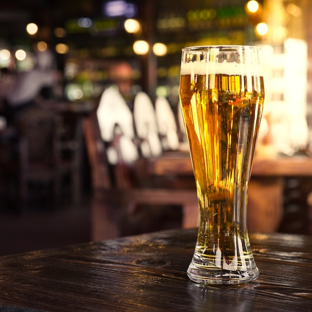 Bicchiere di birra chiara fredda con schiuma sulla scrivania del bar o del pub. Sfondo sfocato di luci bar.