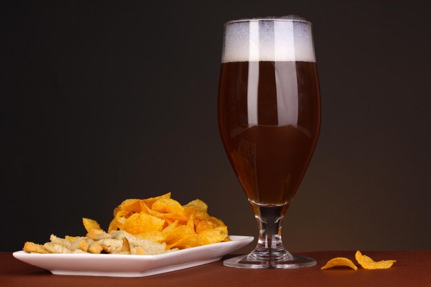 Bicchiere di birra con cracker e patatine su sfondo marrone