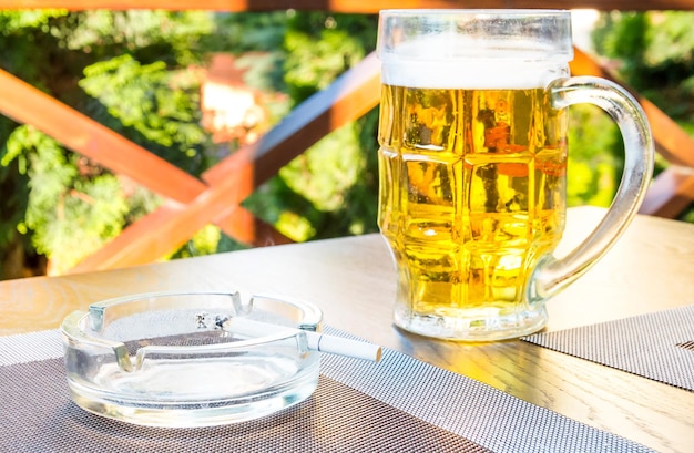 Bicchiere di birra e posacenere con una sigaretta sul tavolo del bar