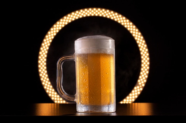 Bicchiere di birra fredda e nebbia intorno su un tavolo nero con un anello di luce sullo sfondo