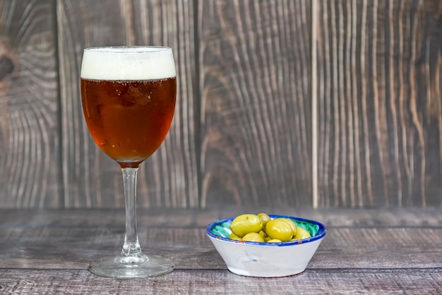 Bicchiere di birra fresca con un tappo di olive verdi Sfondo di legno