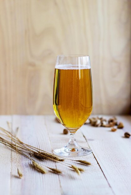 Bicchiere di birra leggera con grano e noci sullo sfondo di legno