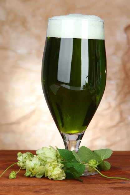 Bicchiere di birra verde e luppolo sulla tavola di legno