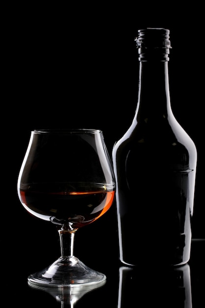 Bicchiere di brandy e bottiglia su sfondo nero