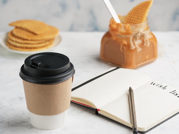 Bicchiere di carta con caffè o bevanda calda sul tavolo. Blocco note con un foglio dei desideri.