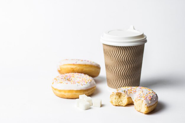 bicchiere di carta con un coperchio, caffè o tè per andare e gustose ciambelle fresche e dolci caramelle decorative multicolori su uno sfondo bianco. Concetto di panetteria, pasticceria fresca, deliziosa colazione, fast food.