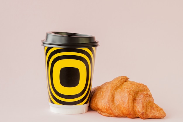 Bicchiere di carta di caffè e croissant su uno sfondo rosa, copia dello spazio.