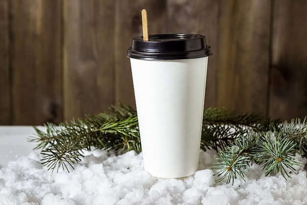 Bicchiere di carta di caffè nella neve con rami di abete.