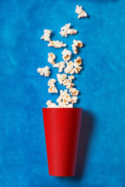 Bicchiere di carta rosso con popcorn sparsi sul blu