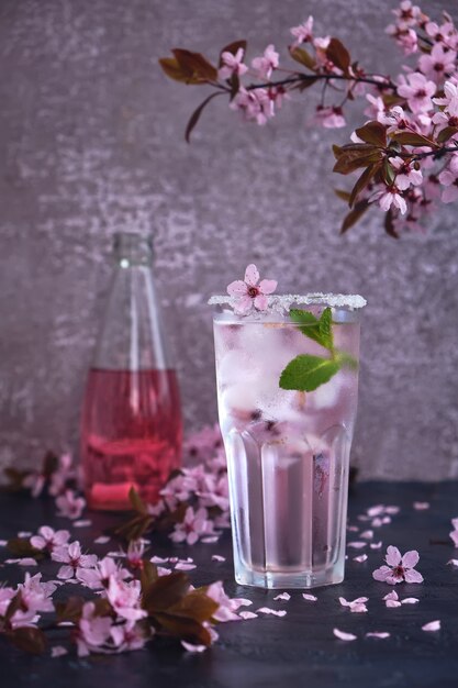 Bicchiere di champagne rosa rosa, sidro o limonata con ghiaccio e menta e fiori di ciliegio