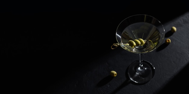 Bicchiere di classico cocktail martini secco con olive sul tavolo di pietra scura su sfondo nero. Con spazio libero per il tuo testo