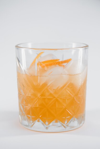 Bicchiere di cocktail Boulevardier con un grosso cubetto di ghiaccio e scorza d'arancia isolato